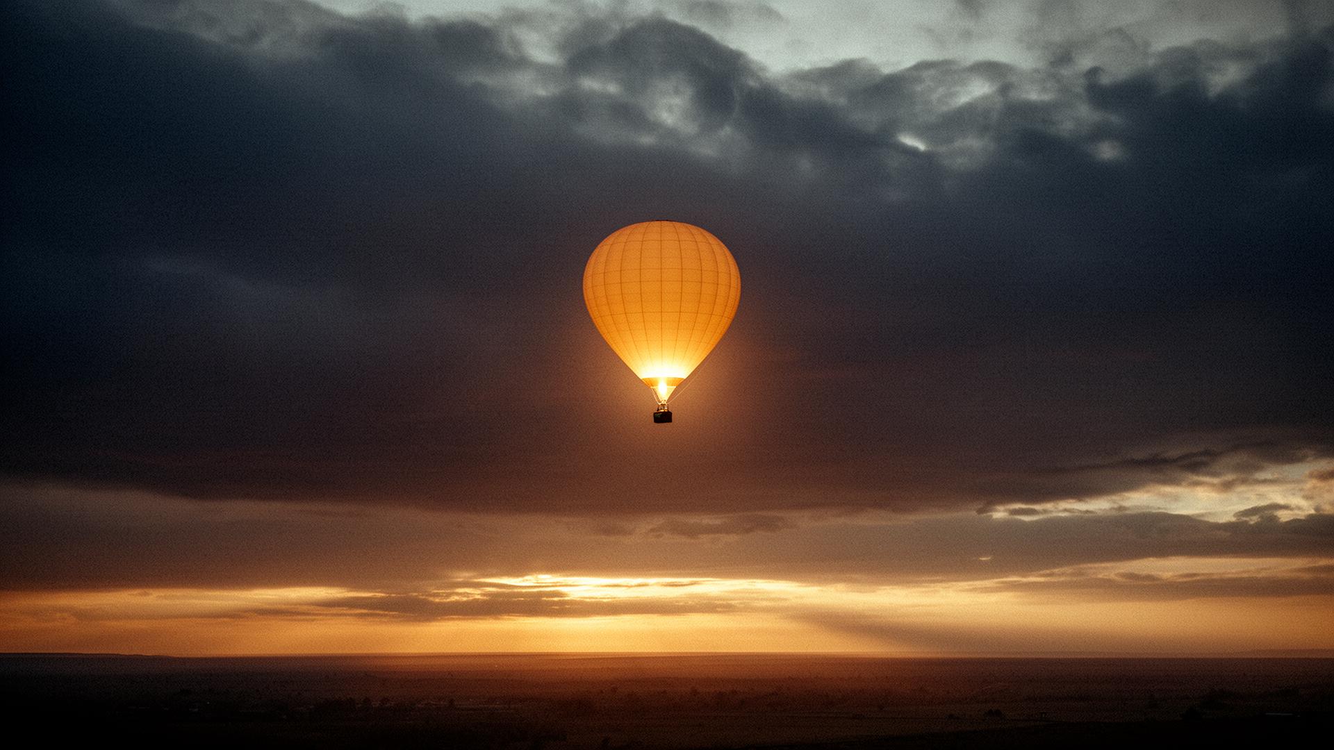 A single luminous hot air balloon drifting through a moody dawn sky